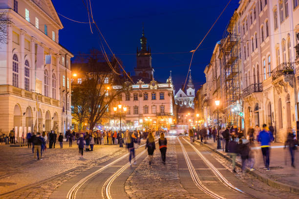 Lviv, Ukraine - October 31, 2018:  view showing people walking around Lviv Old town square, building apartments, trams in the tramway and church tower can be seen on the background at night