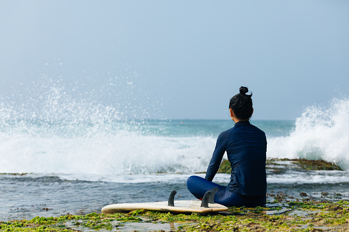 woman surfer sit on reef looking at the waves