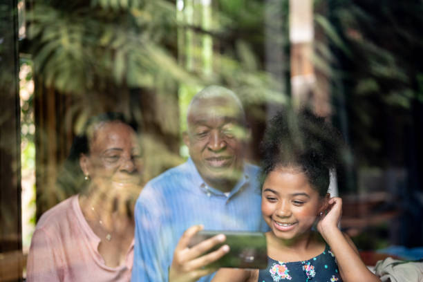 istock Grandparents and Granddaughter Using Mobile Phone Through the Window 1086889704