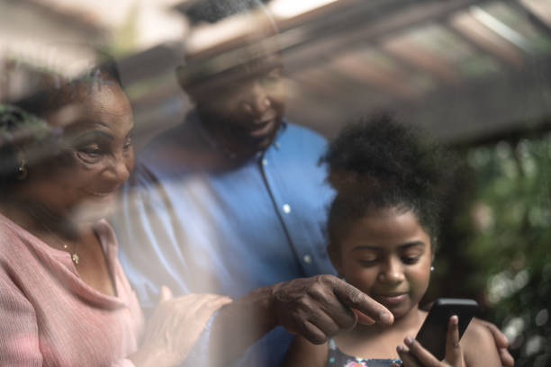 istock Grandparents and Granddaughter Using Mobile Phone Through the Window 1086889706