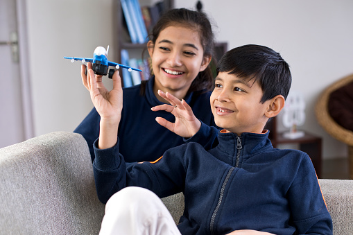 Brother and sister playing with toy airplane at home