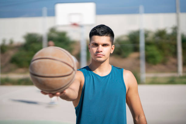 Portrait of a young man holding a basketball ball at the outdoor courtyard.