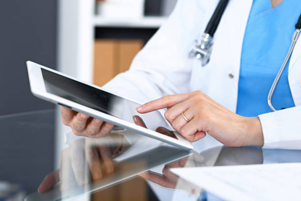 istock Woman doctor using tablet computer while sitting. Reflecting glass table is a working place of physician. Healthcare, insurance and medicine concept. 1086912130