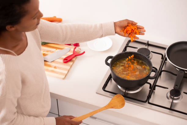 mujer traer el caldo a hervir, agregar zanahorias picadas a la sopa. - cooking domestic kitchen vegetable soup fotografías e imágenes de stock