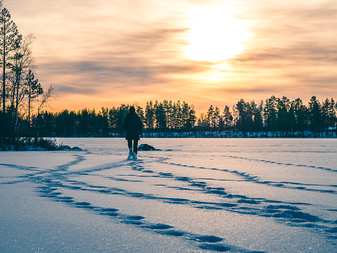 Person is walking on the snowy ice lake in sunset. Winter landscape.