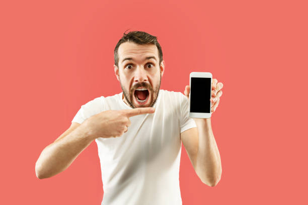 istock Young handsome man showing smartphone screen isolated on coral background in shock with a surprise face 1086940242
