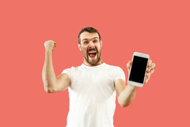 istock Young handsome man showing smartphone screen isolated on coral background in shock with a surprise face 1086940250