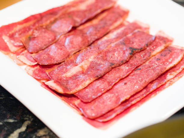 A close up photograph of several sizzling hot turkey bacon slices or pieces on a white serving plate on a kitchen counter ready to eat for breakfast. stock photo