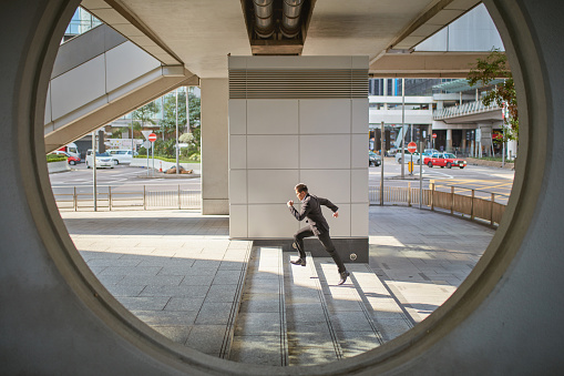 Full length of businessman running on steps. Male professional is getting late in city. He is wearing suit seen through circle.