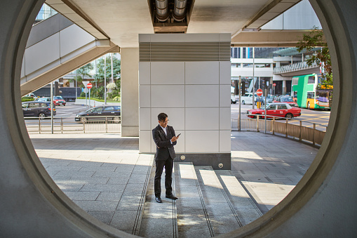 Full length of businessman using mobile phone on steps. Mid adult professional is seen through circle. He is wearing suit while standing in city.