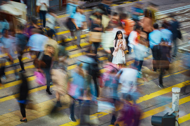 Businesswoman using mobile phone amidst crowd High angle view of young professional using mobile phone amidst crowd. Businesswoman is standing on busy street. She is surrounded by people in city. standing out from the crowd stock pictures, royalty-free photos & images