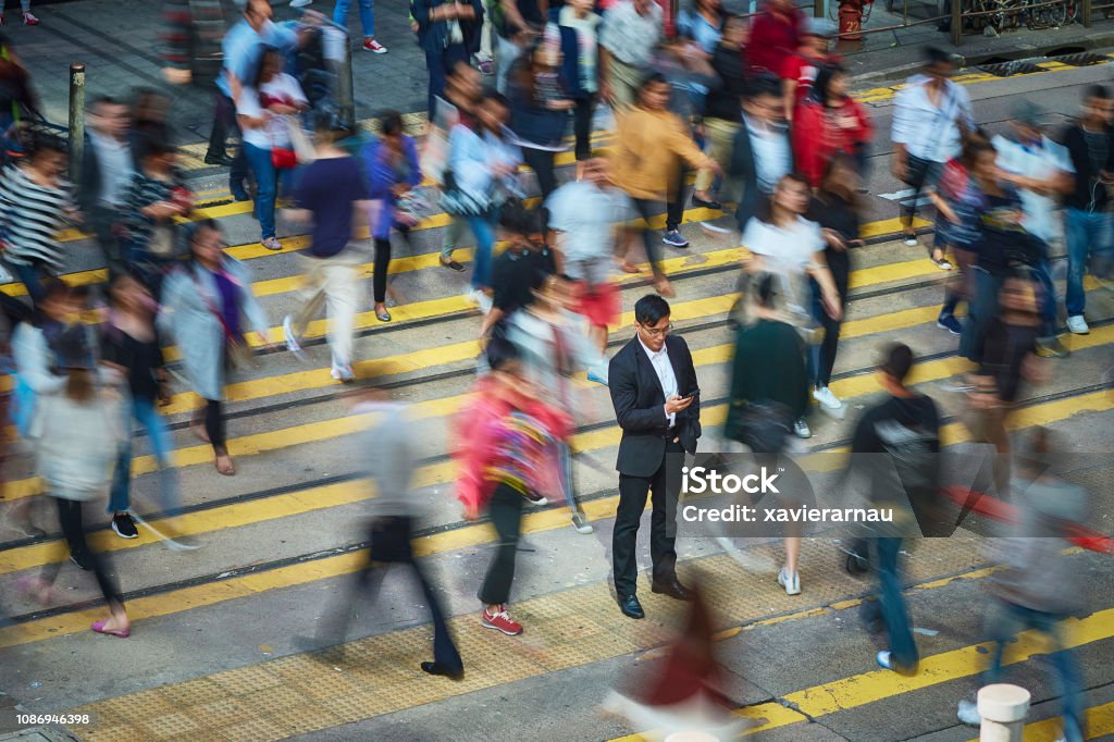 Businessman using smart phone amidst crowd High angle view of businessman using smart phone amidst crowd. Professional is standing on busy street. He is surrounded by people in city. Crowd of People Stock Photo