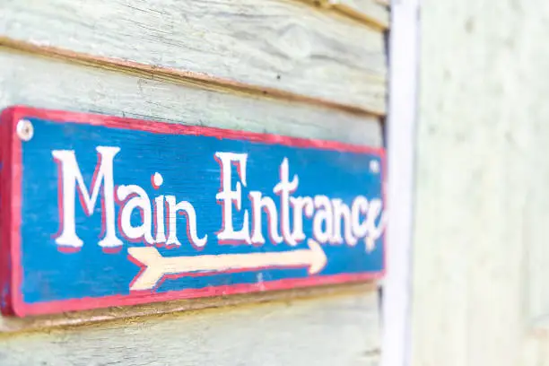 Main entrance sign painted on wooden plank with information, direction arrow in red, white blue on building entrance, entry for restaurant or cafe, small business