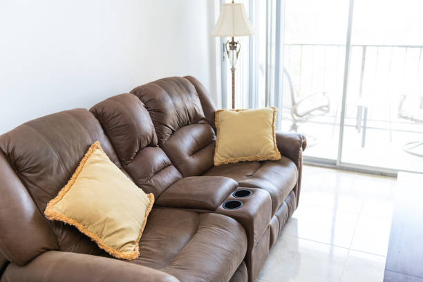 istock Brown leather couch with cushions, lamp, table with bright natural light, balcony in background in house, home apartment living room, tiles, tiled floor 1086958544
