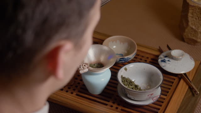 Tea master pours hot water from kettle to gaiwan. Steam from hot cup. Green tea