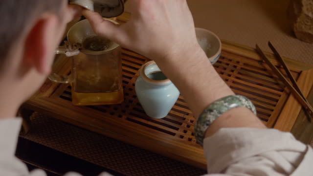 Master pouring green tea infusion from gaiwan in bowl. Chinese tea ceremony