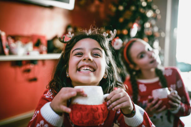 istock Two Little Sisters Playing Around Christmas Tree and Drinking Hot Beverage 1086977354