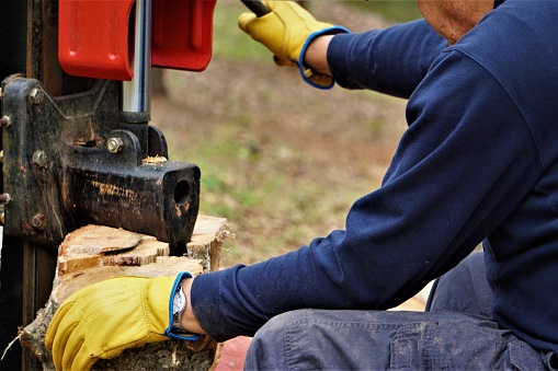 A man working with the firewood to split the logs by the machine on the driveway in the garden, Winter in Georgia USA.