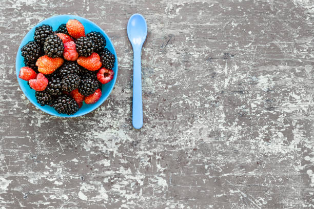 Different berries in blue bowl and a spoon nearby. Top view healthy concept with organic tasty berries and place for text