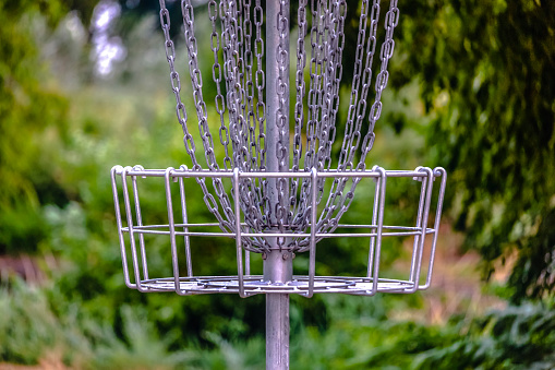 The target basket of Frisbee golf or Disc Golf. Close up view of a frisbee golf or disc golf target on a course in Provo, Utah against a blurry background. The target has metal chains and a basket.