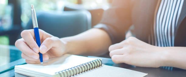 istock Woman writing on a notebook with a pen in the office.Web banner. 1087073202