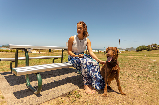 Young Woman Relaxing at Picnic Table at the Beach With Her Dog