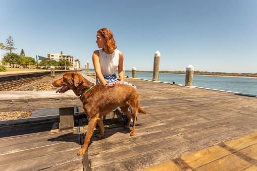 Young woman sitting on a pier in a river with her dog