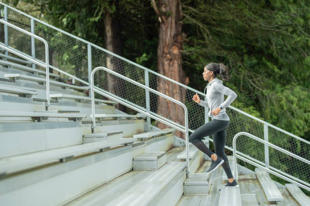 Female track athlete trains on stadium bleachers An African American female track athlete trains at a stadium. She is in profile as she runs up the bleachers. cardiovascular exercise stock pictures, royalty-free photos & images