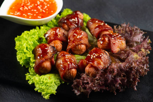 istock Pigs in blankets. Mini sausages wrapped in smoked bacon in baking dish 1087117836