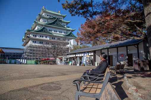 Nagoya, Japan - December 2018 : Girl sitting and looking to Nagoya Castle in winter. Famous castle in Japan with green roof. Located in 1-1 Hommaru, Naka, Nagoya, Aichi Prefecture, Japan. This castle was reconstructed in 1959.