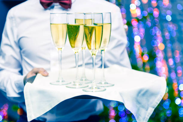 официант, обслуживающий бокалы шампанского на подносе в ресторане. nice bokeh рождественские огни и елки в фоновом режиме. - butler champagne service waiter стоковые фото и изображения