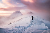 Man mountaineer walking with snow footprint on snow peak ridge in blizzard