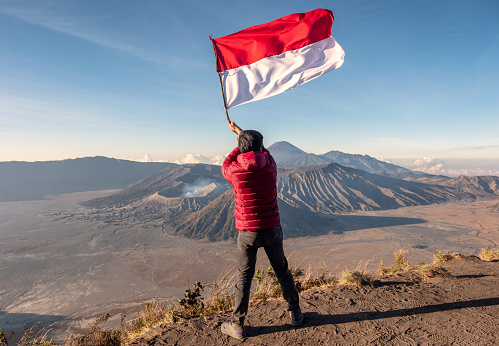 Man waving the flag of Indonesia on top of mountain with bromo volcano background at morning