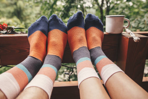 calze eleganti su gambe di coppia e tazza di metallo su portico in legno con vista sui boschi in montagna. famiglia felice che si rilassa insieme, momento di unione. buffi calzini carini - balcony human foot men relaxation foto e immagini stock