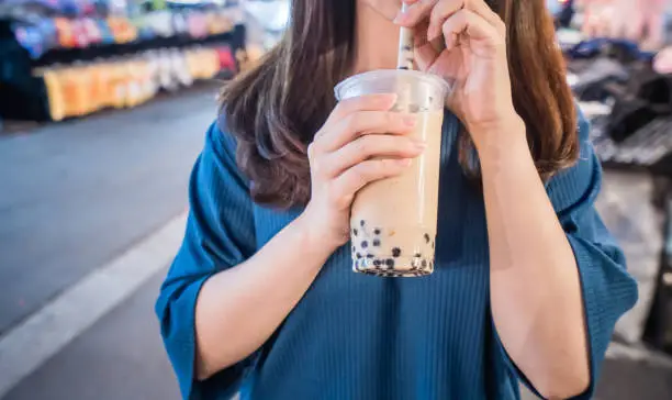 Photo of A young woman is drinking a plastic cup of bubble milk tea with a straw at a night market in Taiwan, Taiwan delicacy, close up.