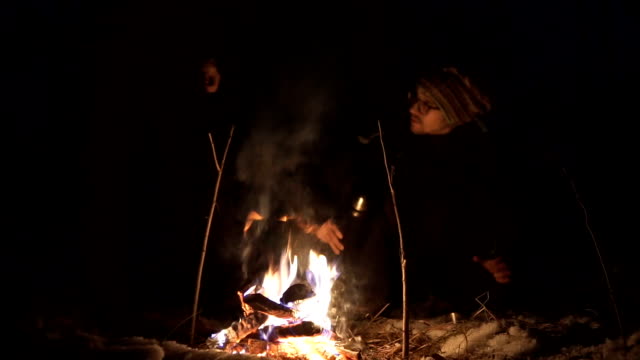 Two friends in the winter season of the year at night in the woods make a fire, and drink tea