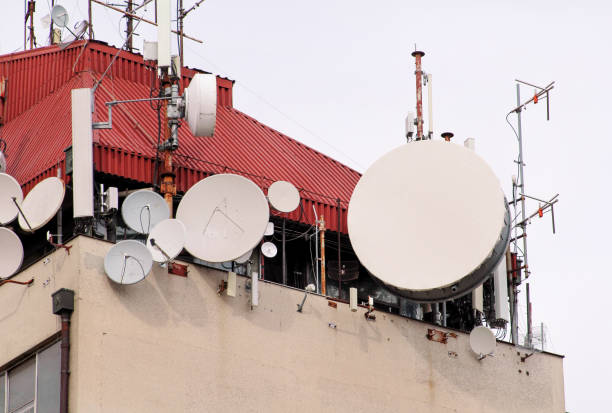 istock Telecommunication base stations network repeaters on the roof of building. The cellular communication aerial on city building roof. Cell phone telecommunication tower. Antennas on top of building. 1087212676