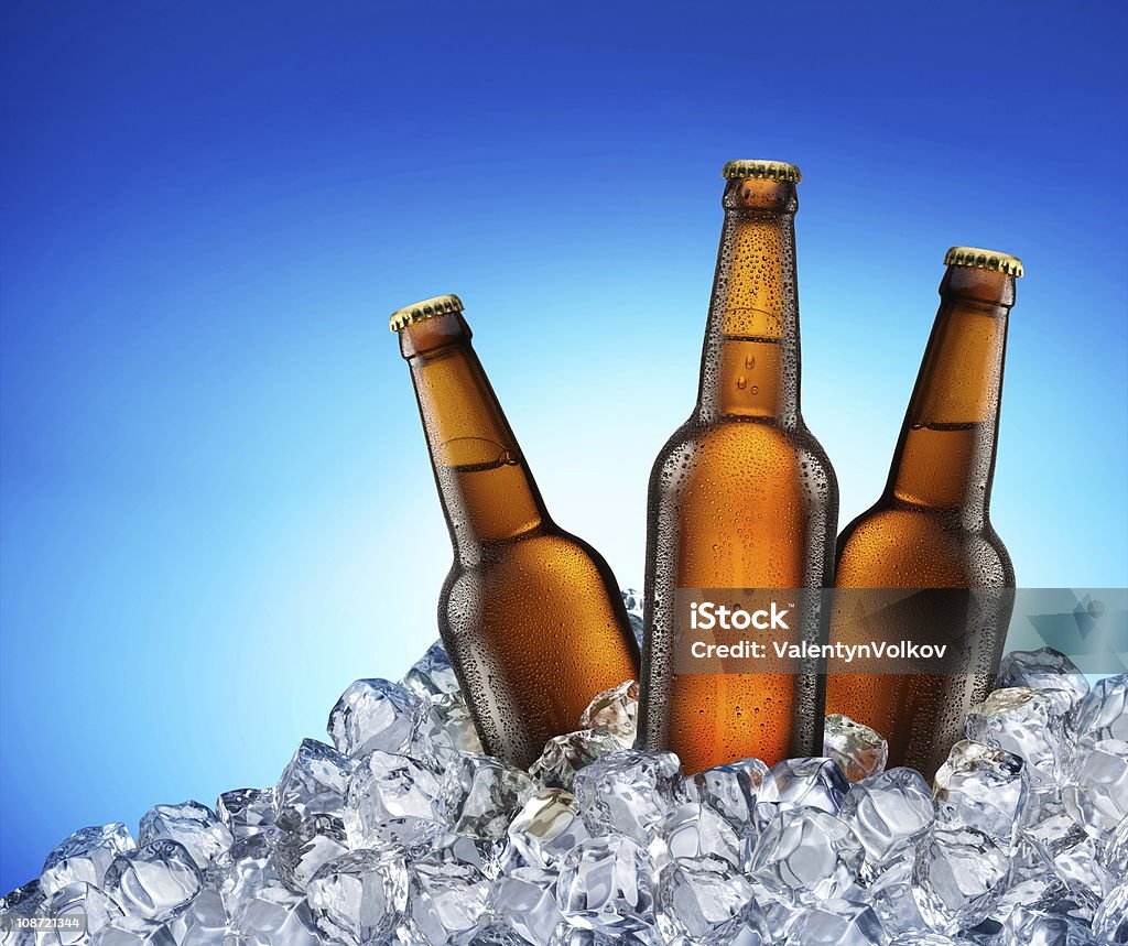 Cool beer bottles. Three beer bottles getting cool in ice cubes. Isolated on a blue. File contains a path to cut Ice Stock Photo