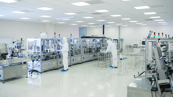 Shot Of Sterile High Precision Manufacturing Laboratory where Scientists in Protective Coverall's Use Computers and Microscopes, doing Pharmaceutics, Biotechnology and Semiconductor Research.