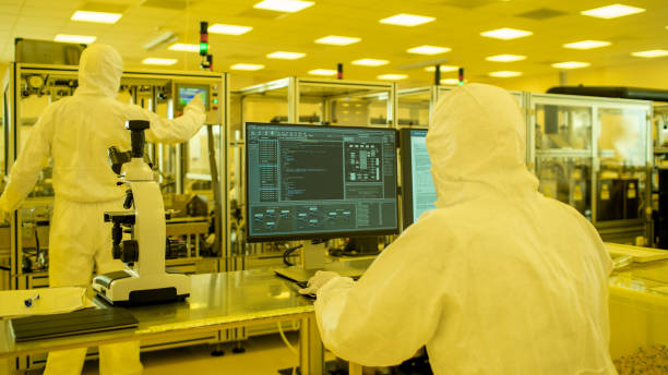 tiro de um cientistas em estéril ternos trabalhar com computadores, analisando dados forma a maquinaria industrial moderna no laboratório. processo de fabricação do produto: farmácia, semicondutores, biotecnologia. - máquina de manufactura farmacêutica - fotografias e filmes do acervo