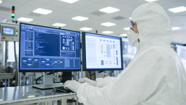 istock Shot of Scientists in Sterile Suits Working with Computers, Analyzing Data form Modern Industrial Machinery in Laboratory. Product Manufacturing Process: Pharmaceutics, Biotechnology. Yellow Filter. 1087218922