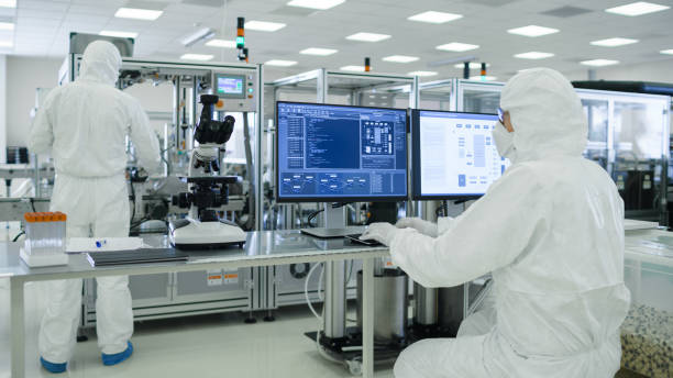 istock Shot of a Scientists in Sterile Suits Working with Computers, Analyzing Data form Modern Industrial Machinery in the Laboratory. Product Manufacturing Process: Pharmaceutics, Semiconductors, Biotechnology. 1087218962