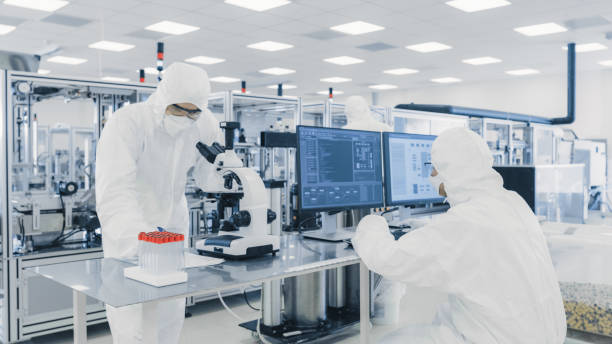 istock Team of Research Scientists in Sterile Suits Working with Computers, Looking Under Microscope and Modern Industrial Machinery in the Laboratory. Product Manufacturing Process: Pharmaceutics, Semiconductors, Biotechnology. 1087218990