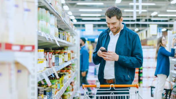 istock At the Supermarket: Handsome Man Uses Smartphone and Stands in Canned Goods Section. He's Looking for a Best Healthy Product. 1087219032