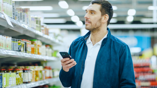 istock At the Supermarket: Handsome Man Uses Smartphone, Smiles while Standing at the Canned Goods Section. 1087219120