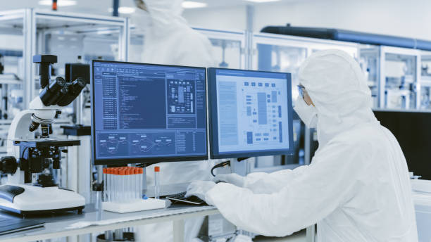 im labor über die schulter-blick des wissenschaftlers in schutzkleidung forschen auf einem personal computer. moderne manufaktur herstellung von halbleitern und pharmazeutische artikel. - biotechnology factory industry technology stock-fotos und bilder