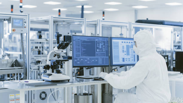 istock In Laboratory Over the Shoulder View of Scientist in Protective Clothes Doing Research on a Personal Computer. Modern Manufactory Producing Semiconductors and Pharmaceutical Items. 1087219242