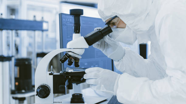 istock In Laboratory Scientist in Protective Clothes Doing Research Uses Microscope and Personal Computer. Modern Manufactory Producing Semiconductors and Pharmaceutical Items. 1087219268