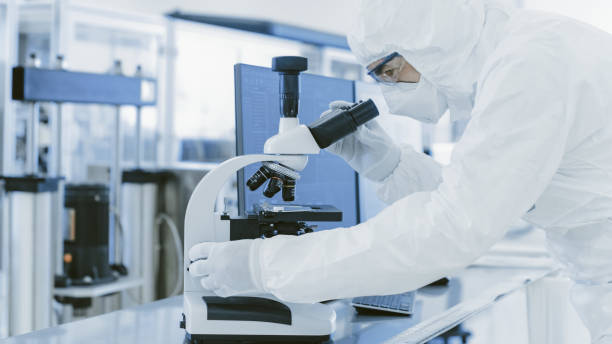 istock In Laboratory Scientist in Protective Clothes Doing Research Uses Microscope and Personal Computer. Modern Manufactory Producing Semiconductors and Pharmaceutical Items. 1087219288