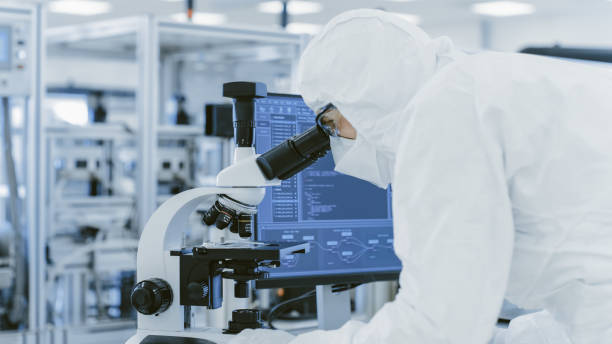 istock In Laboratory Scientist in Protective Clothes Doing Research Uses Microscope and Personal Computer. Modern Manufactory Producing Semiconductors and Pharmaceutical Items. 1087219298